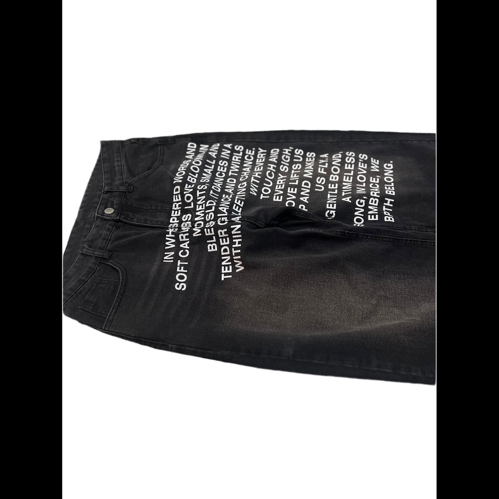 Black denim jeans with white printed text on the front, laid flat on a white background.