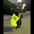 A person on a motorcycle at night wearing a bright yellow safety vest with 'ACE STUDIOS' printed on the back, riding on a street.