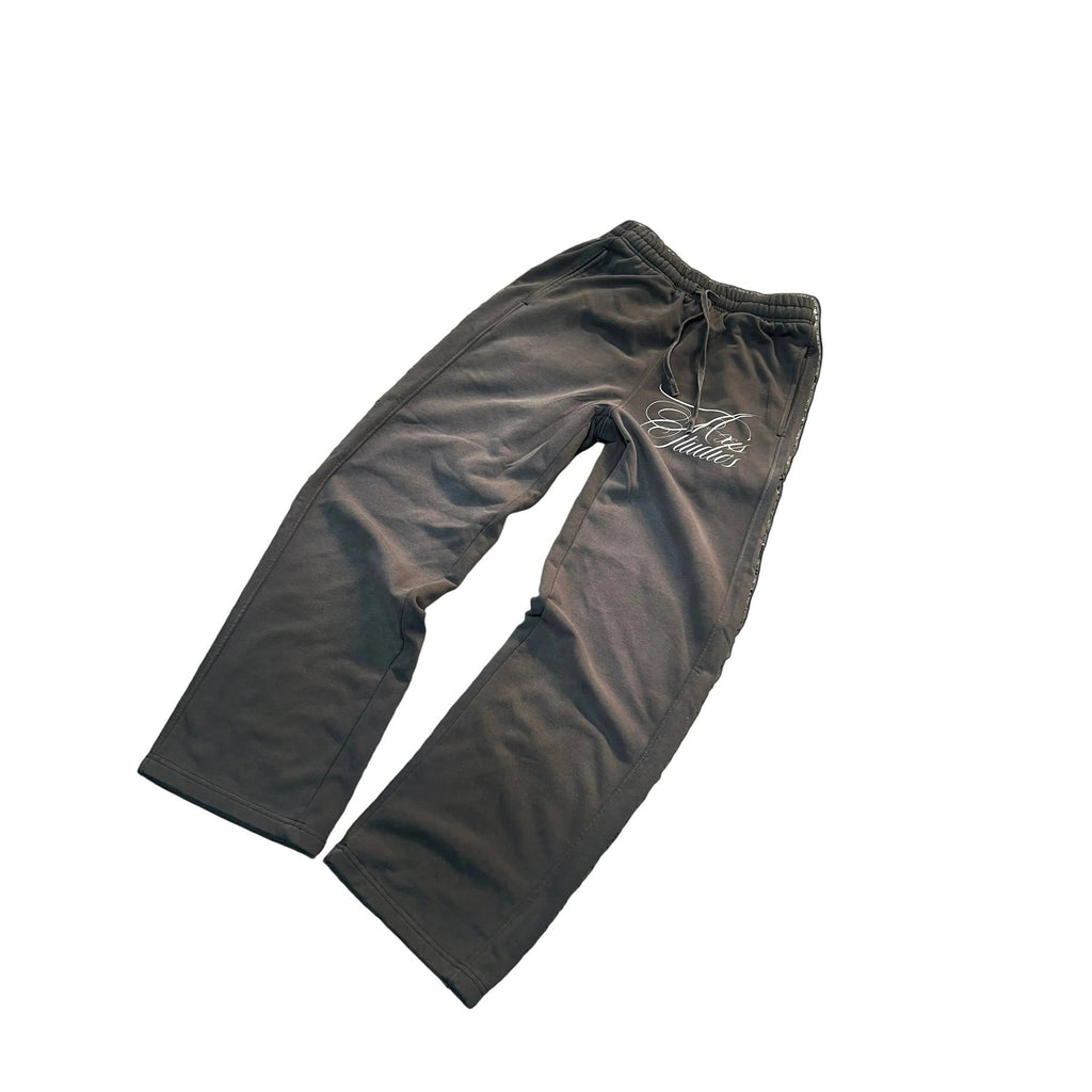 A pair of dark gray drawstring sweatpants with a white script logo on the upper left thigh, displayed flat against a white background with black letterbox bars on the sides.