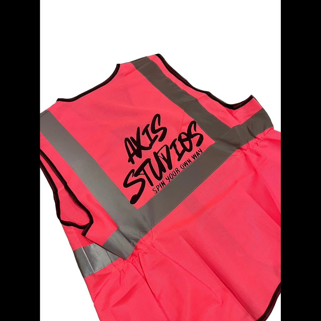 A neon pink high-visibility safety vest with reflective gray stripes and black trim, featuring the custom printed logo 'AKS STUDIOS' on the back.