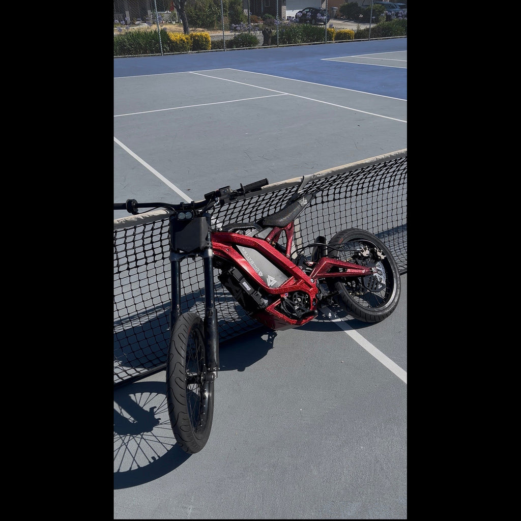 A red electric bicycle with a black frame and black tires, parked on a blue court behind a net.