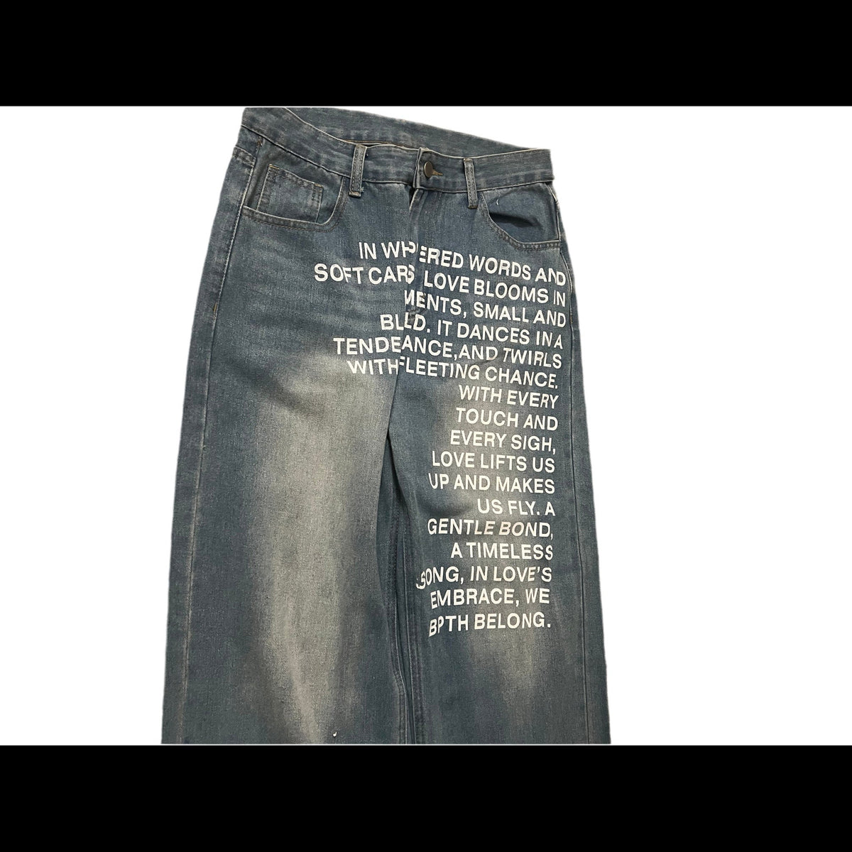 A pair of faded blue denim jeans laid flat on a white background, rotated sideways. The front of the jeans features white printed text on the thigh.