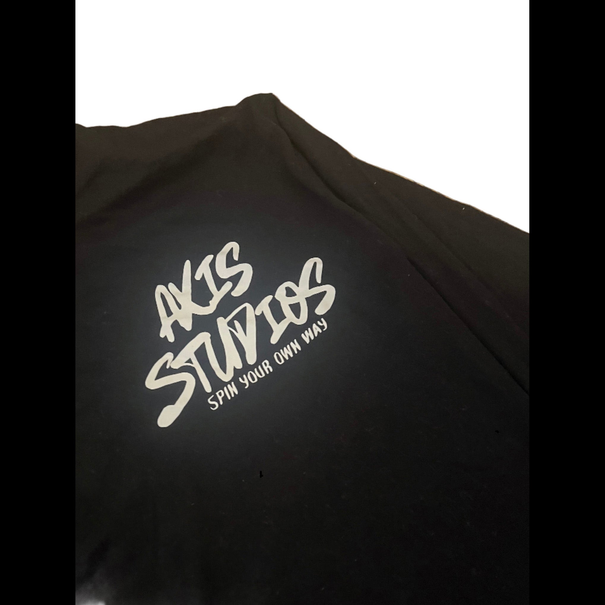 A close-up of a black t-shirt featuring a white graphic print that reads 'AXIS STUDIOS' and 'SPIN YOUR OWN WAY!' on the chest.