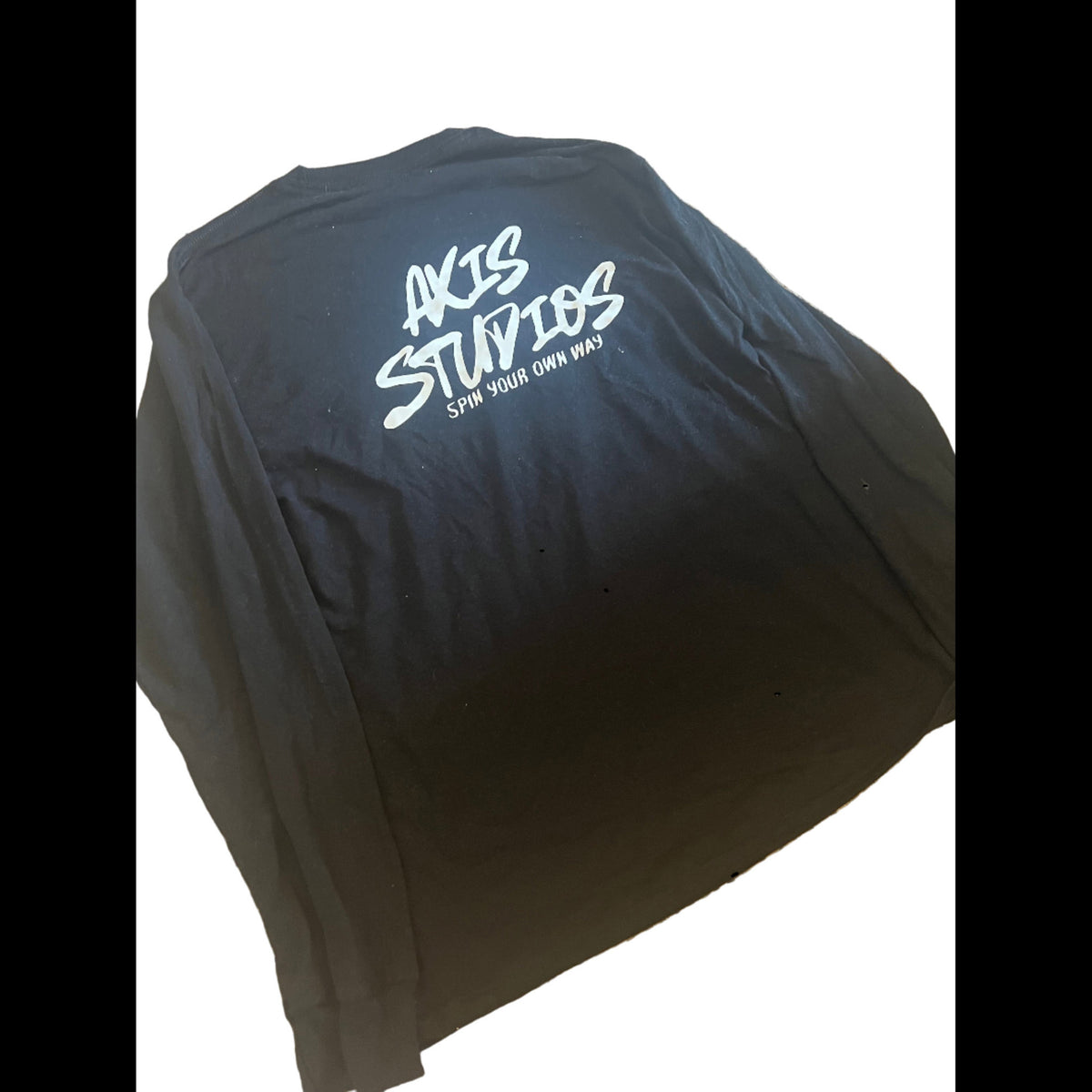 A black long-sleeve t-shirt with a white graphic print on the back reading 'AKIS STUDIOS' and 'SHOW YOUR OWN WAY', displayed on a white background.