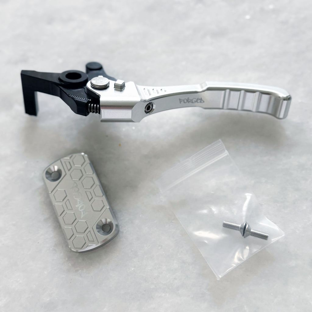 A silver and black bicycle crank arm with a hexagonal metal cover and a small plastic bag containing a bolt, displayed on a light gray textured surface.