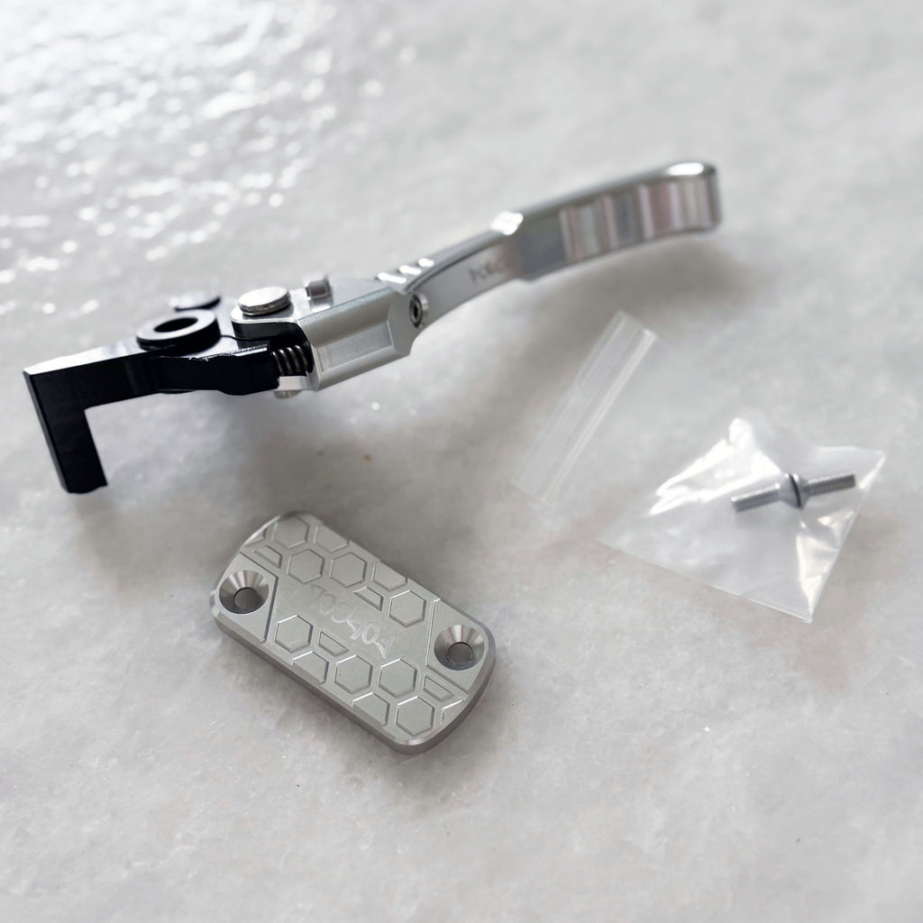 A silver and black metal bicycle headset component shown on a light gray textured surface, alongside a matching silver hex-patterned cover plate and a small clear plastic bag containing a screw.