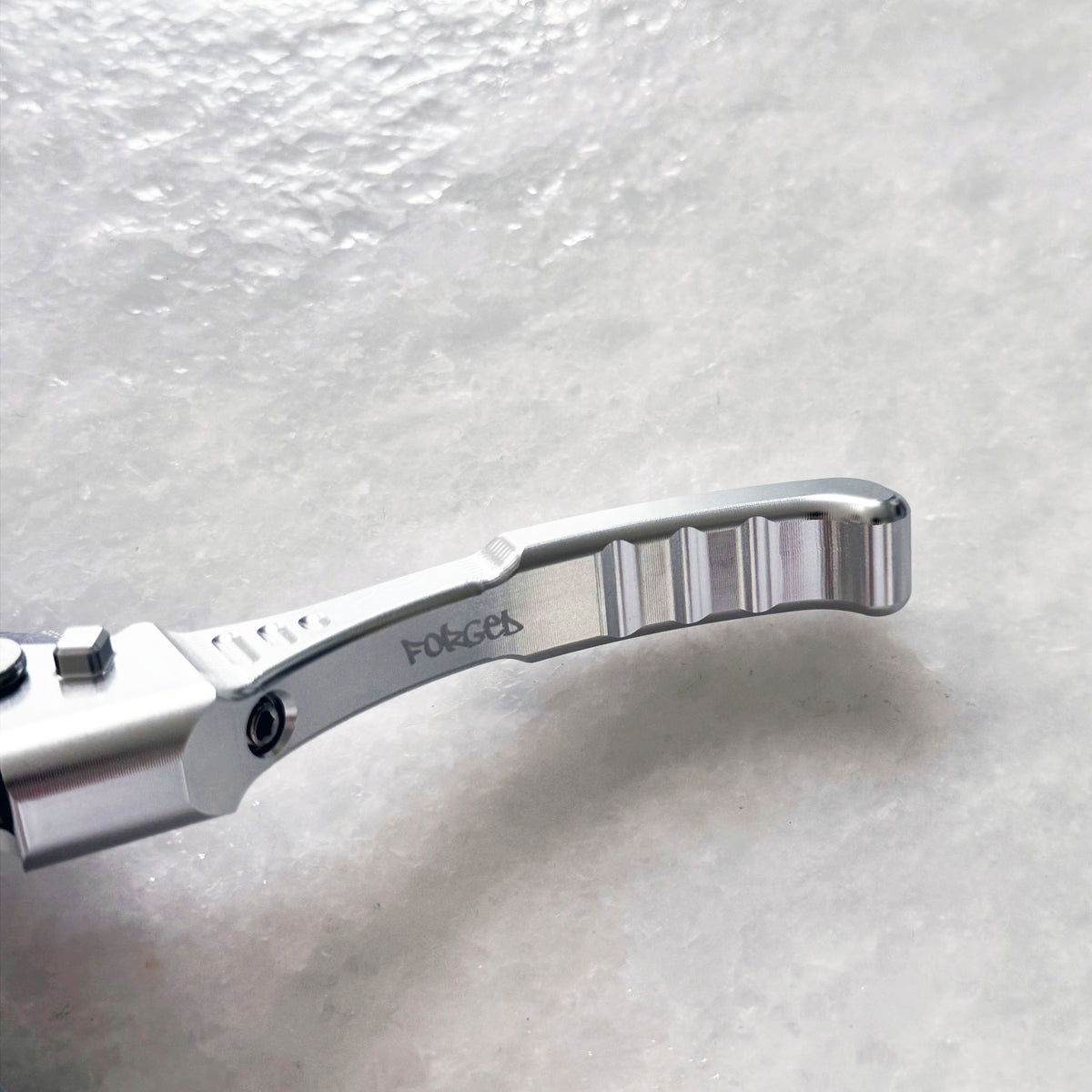 Close-up of a silver metallic bicycle crank arm with the brand name 'FocEes' engraved on it, resting on a textured white surface.